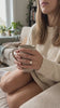 Round Solitaire Ring worn while holding a mug on the sofa